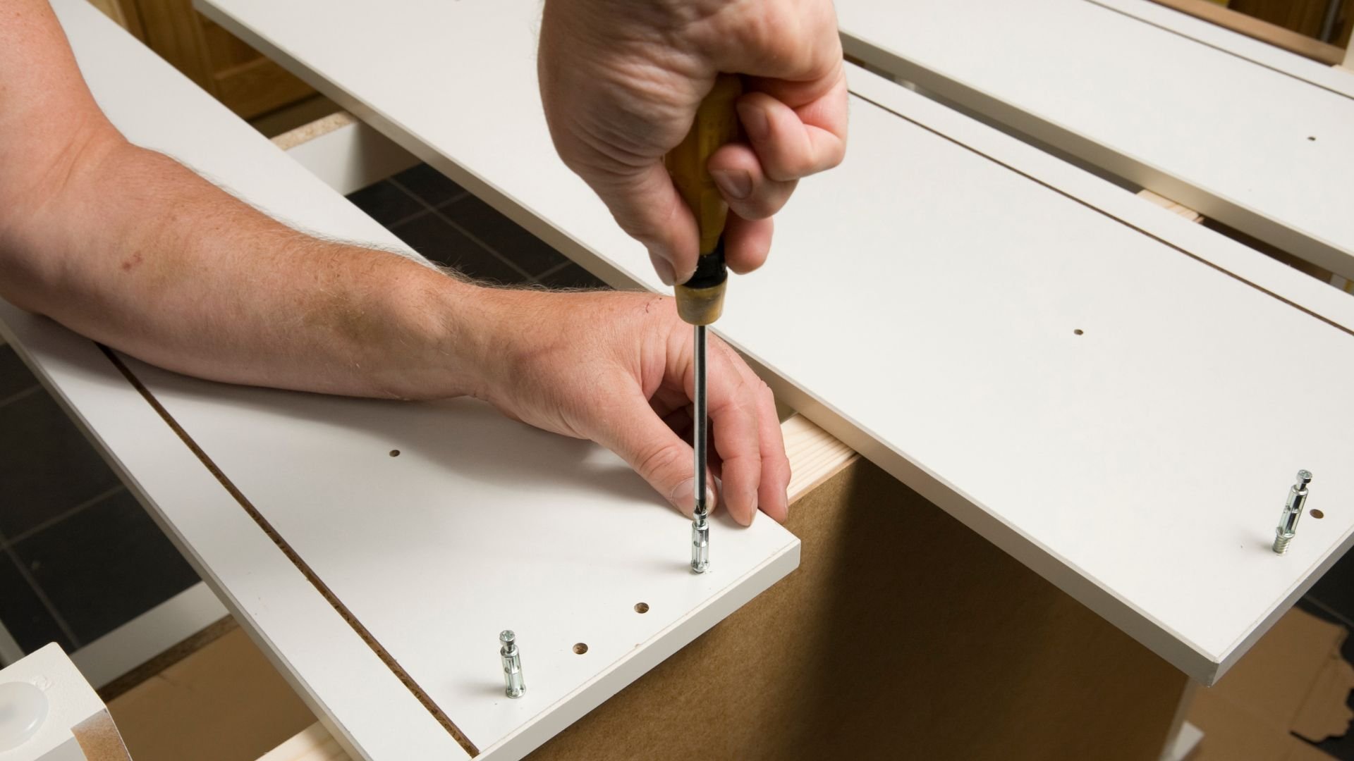Hand using screwdriver to assemble white wooden furniture pieces