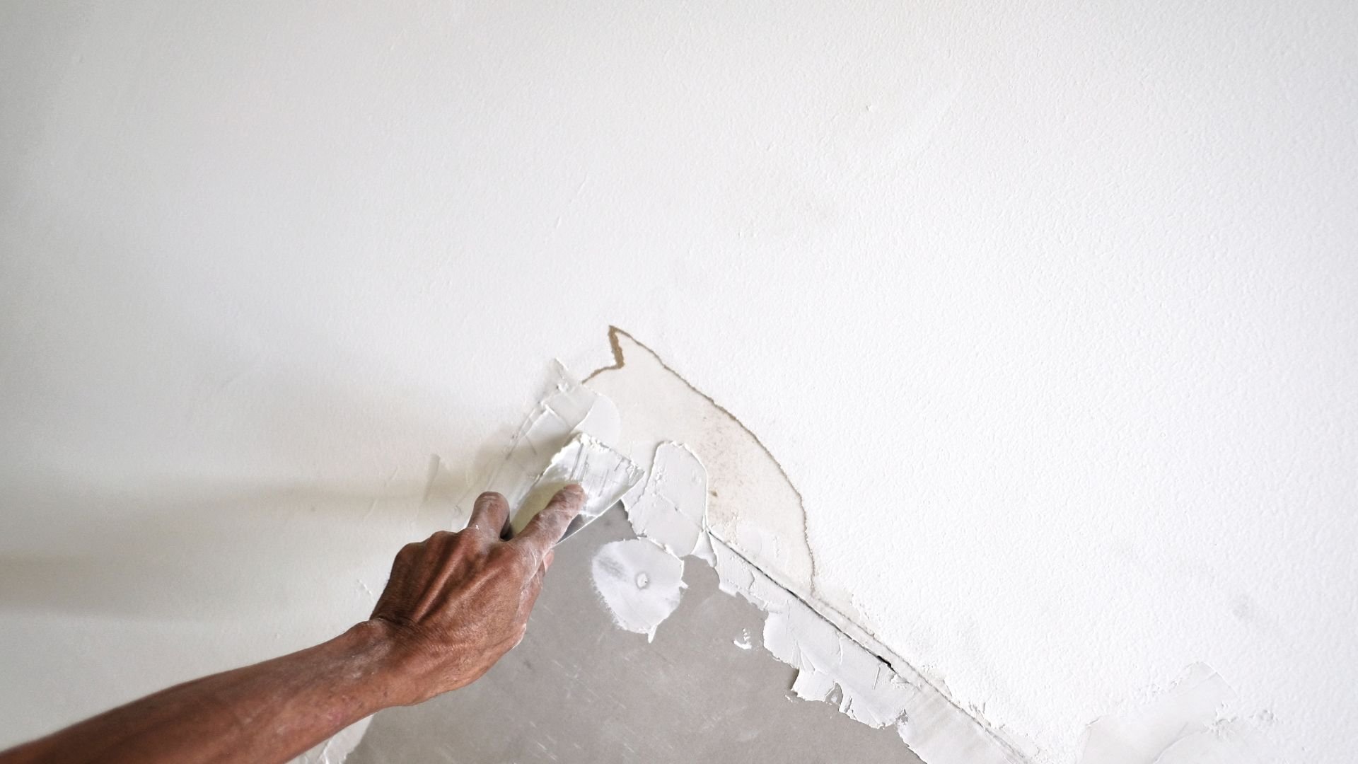 Hand peeling damaged wallpaper from white wall during home renovation